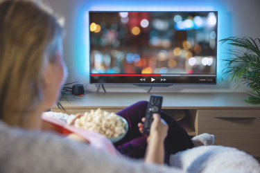Eine Frau sitzt mit Popcorn vor dem Fernseher und streamt ein Video (Bildquelle: Kaspars Grinvalds - stock.adobe.com)
