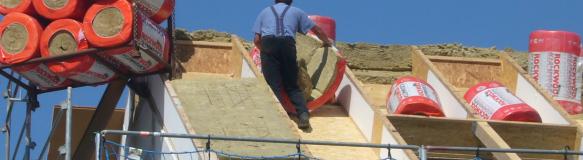 Ein Dach wird von einem Handwerker mit einer dicken Schicht Steinwolle gedämmt (Quelle: Dr. Josef Hochhuber)