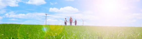 Das Symbolbild soll Akzeptanz von erneuerbaren Energien darstellen und zeigt eine Familie auf einer Wiese und Windräder im Hintergrund (Bildquelle: M.studio - stock.adobe.com)