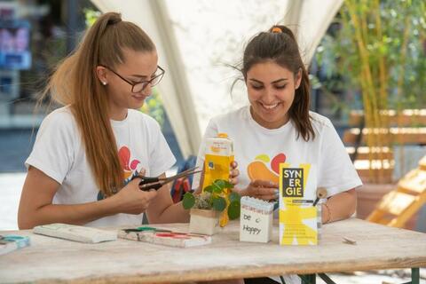 Zwei junge Frauen basteln Nützliches aus gebrauchten Getränkekartons. (Quelle: Armin Weigel)