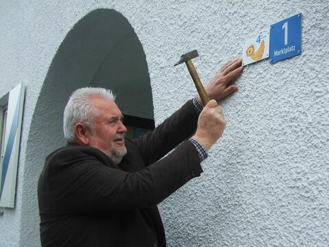 Martin Esterl (Bürgermeister in Glonn 1996 - 2014) befestigt die Plakette am Rathaus in Glonn. (Quelle: Renate Glaser)