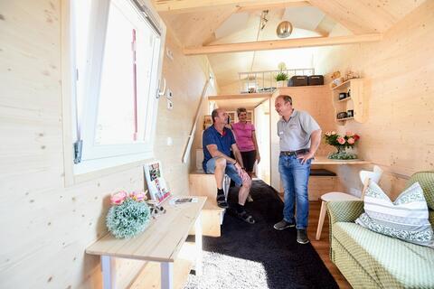 Drei Personen stehen im Tiny-Haus der Zimmerei Prommersberger weit hinten im Gespräch miteinander. Das Haus ist ganz aus warmem hellem Holz. (Quelle: Tobias Hase) So gemütlich kann es auf engstem Raum zugehen - das Tinyhouse der Zimmerei Prommersberger. (Quelle: Tobias Hase)