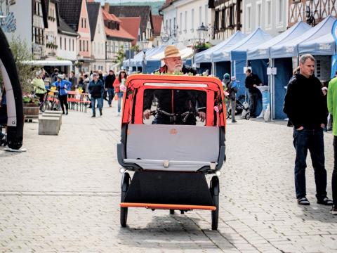 Ein grauhaariger Mann mit Hut fährt mit einem Lastenfahrrad zwischen den Ständen des Energiesparfestivals (Quelle: Oliver Kordes) 