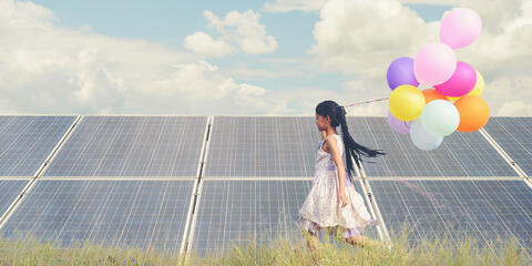 Ein Mädchen mit bunten Luftballons läuft vor einer Freiflächen-Photovoltaikanlage. Energiebildung für Kinder und Jugendliche ist sehr wichtig (Quelle: Palidachan - Adobe Stock)
